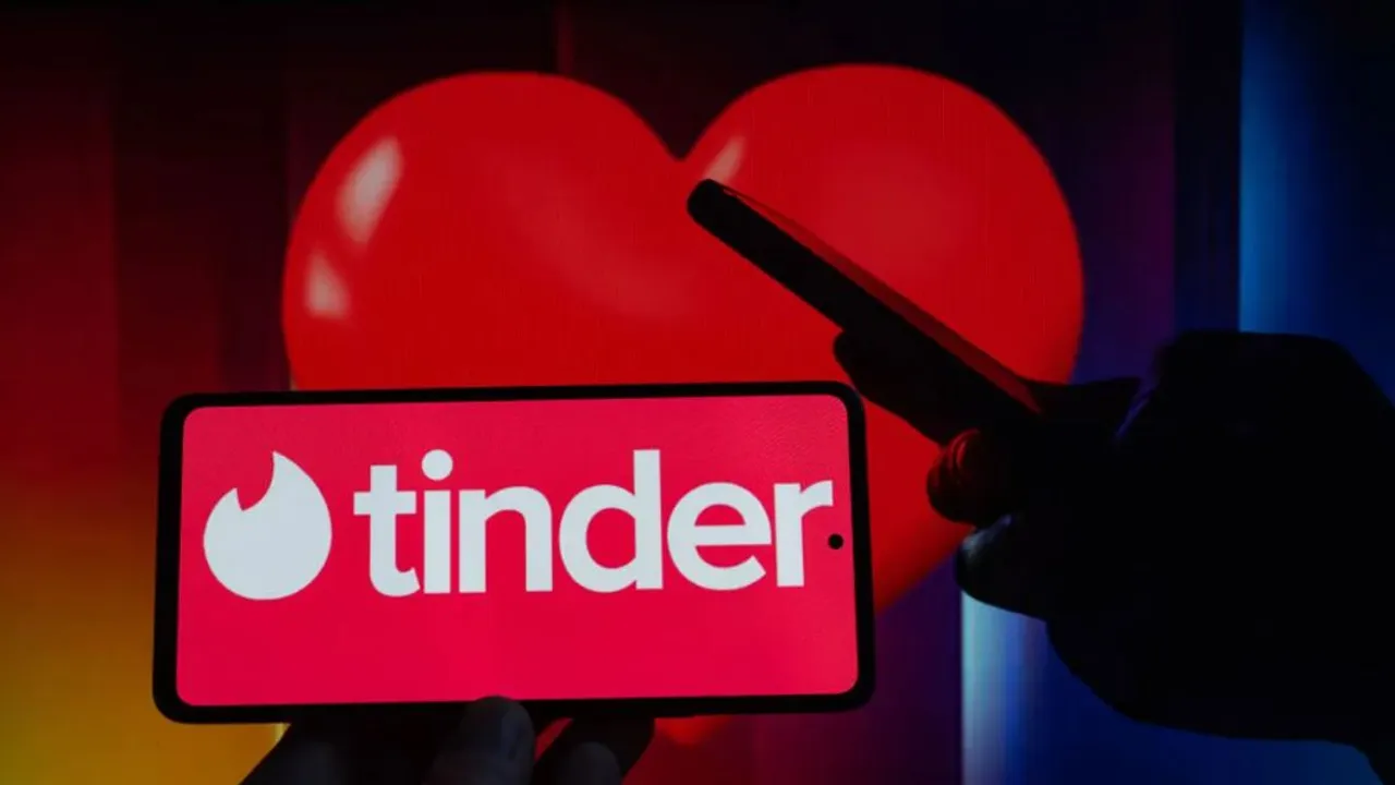 Mano sosteniendo un teléfono con la pantalla roja que muestra el logo blanco de la aplicación Tinder