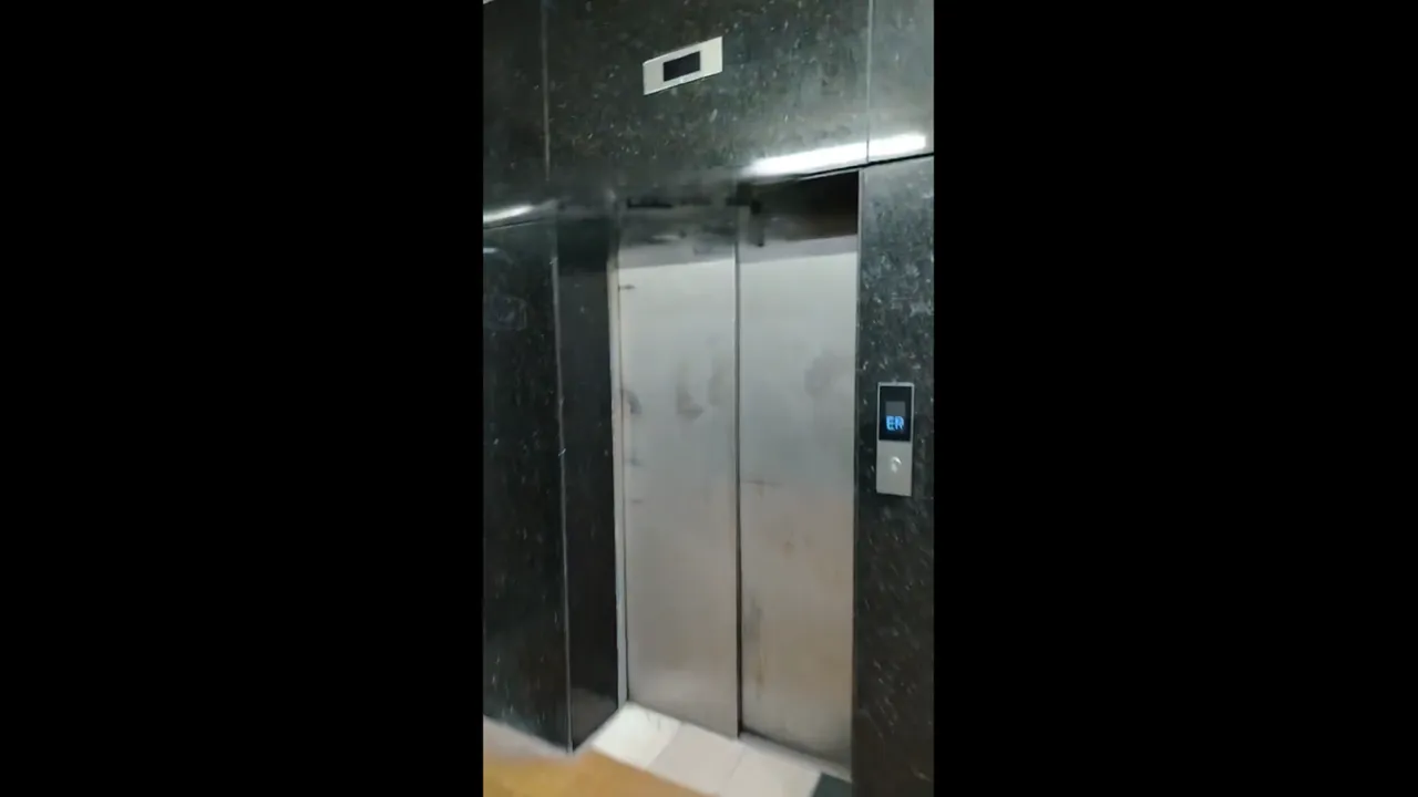 Puertas metálicas cerradas de un ascensor con marco de mármol oscuro en un pasillo hospitalario.