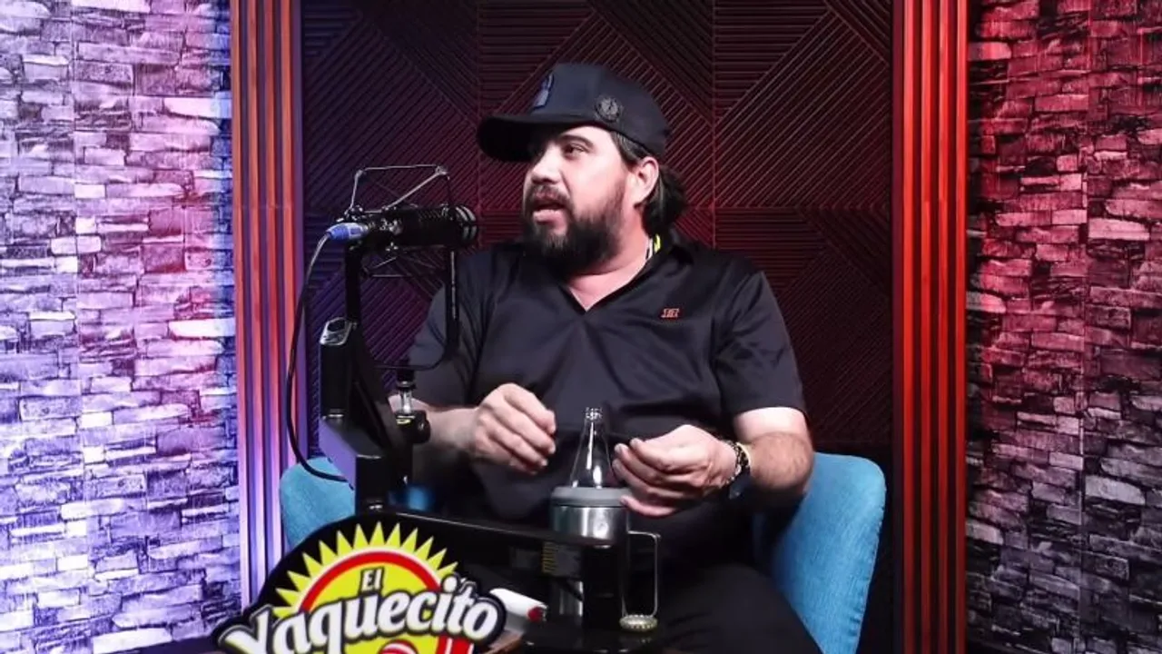 Hombre con gorra oscura y barba hablando frente a un micrófono en el estudio de un programa de pódcast.