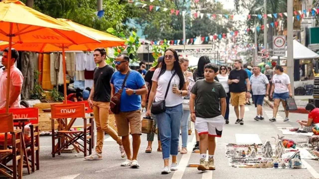 Personas caminan por una calle peatonal decorada con banderas y puestos de venta al aire libre