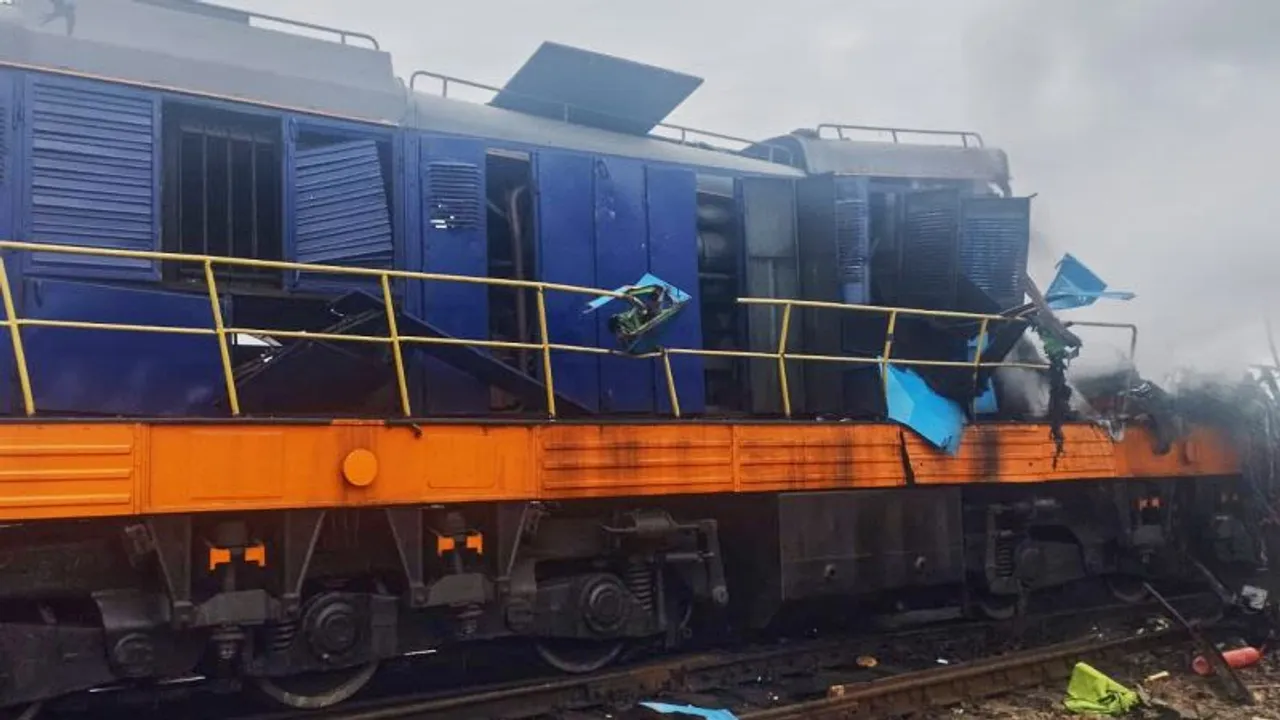 Locomotora azul y naranja destrozada con paneles de metal retorcidos y humo en una vía ferroviaria.