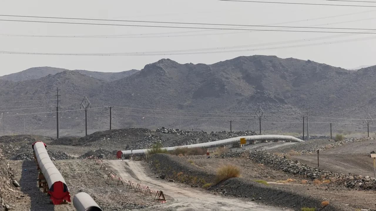Tuberías de un oleoducto extendidas a través de un terreno desértico y pedregoso con montañas al fondo
