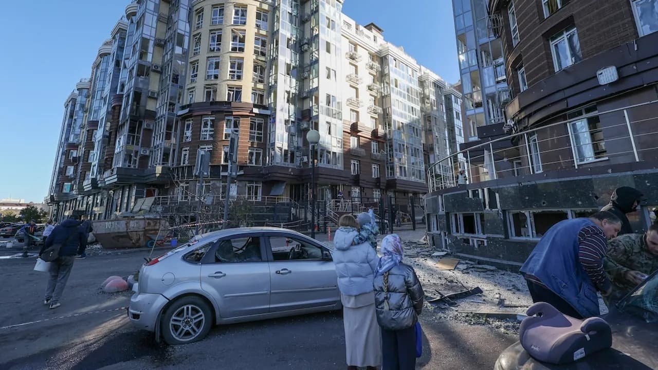 Edificio de departamentos con ventanas rotas y autos dañados por escombros tras un ataque en una calle urbana.