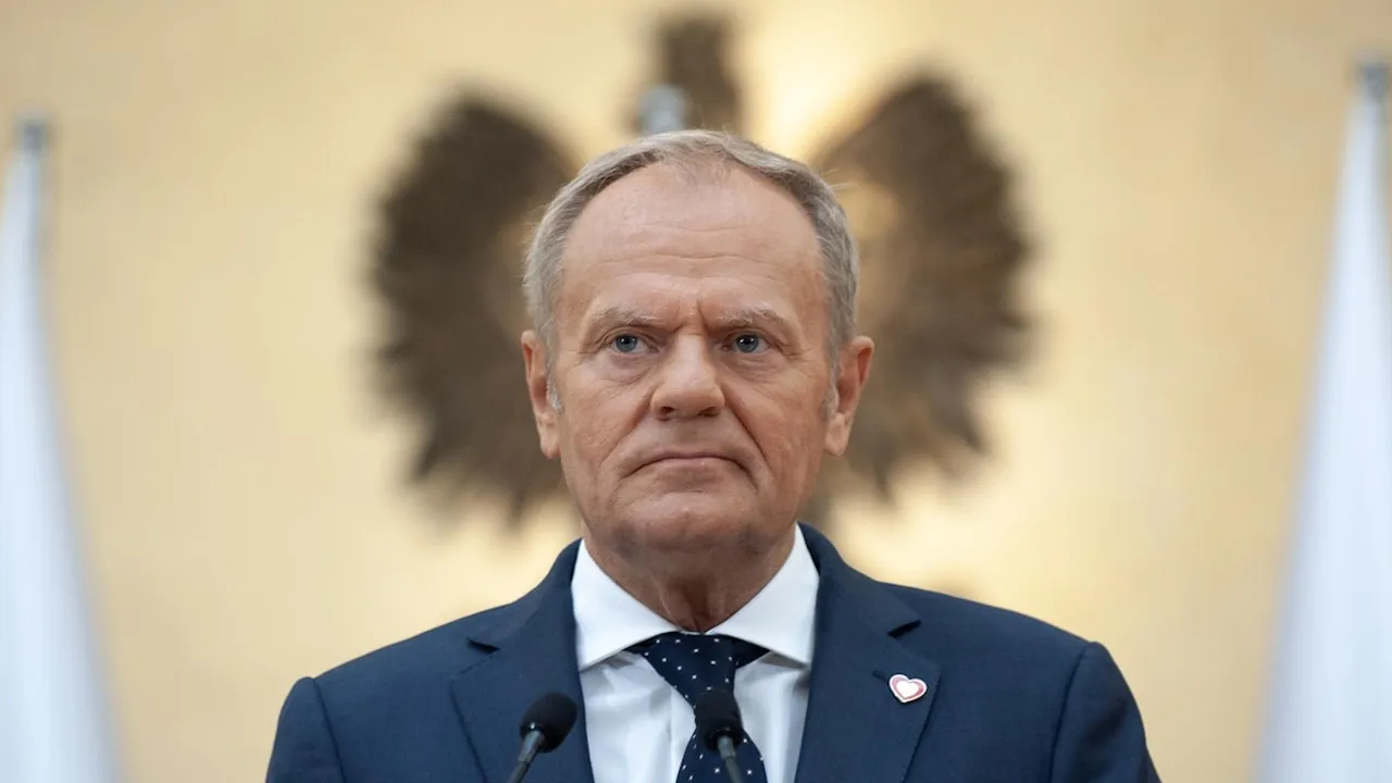 Donald Tusk con traje oscuro frente a micrófonos oficiales y el emblema nacional polaco difuminado detrás