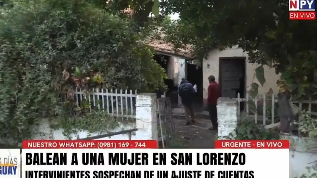 Agentes policiales y vecinos frente a la entrada de una modesta vivienda con verja blanca en San Lorenzo.