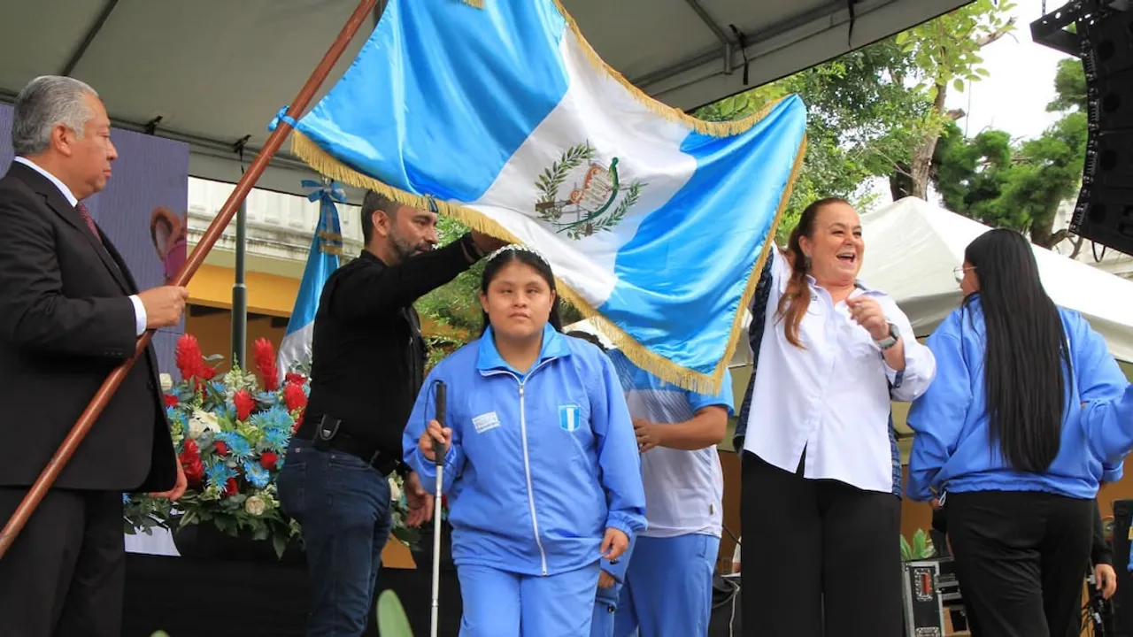 Joven deportista con bastón blanco frente a la bandera de Guatemala sostenida por directivos en un escenario.