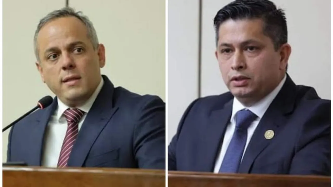 Dos hombres en traje y corbata sentados en una mesa oficial con micrófonos durante una sesión parlamentaria.