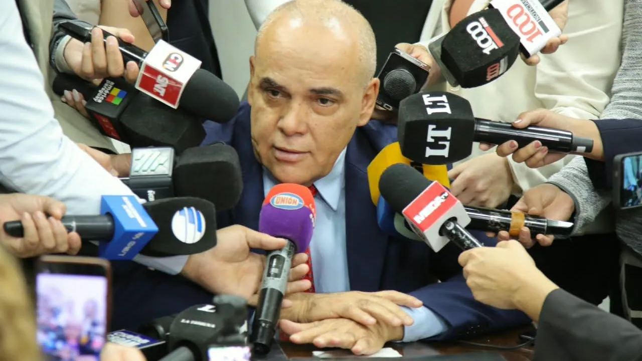 Basilio Núñez de traje azul rodeado por numerosos micrófonos de medios de prensa.