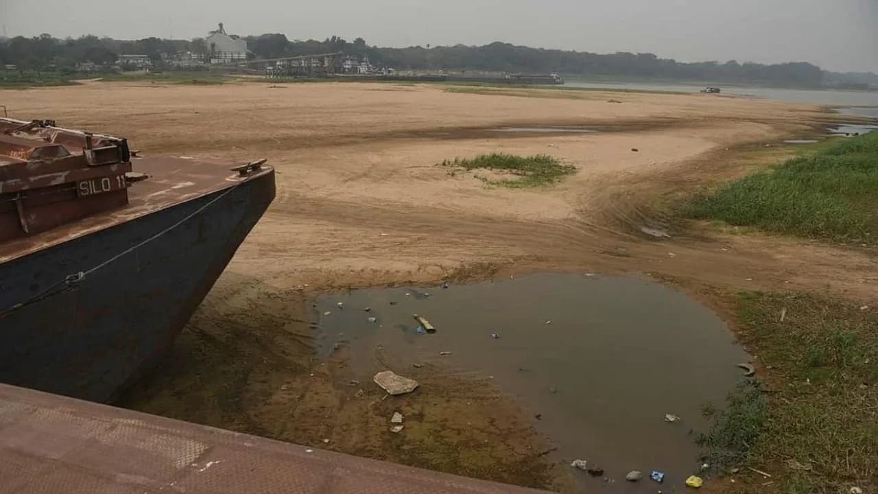 Embarcación varada junto a un extenso banco de arena y charcos en la ribera debido al bajo nivel del cauce hídrico.