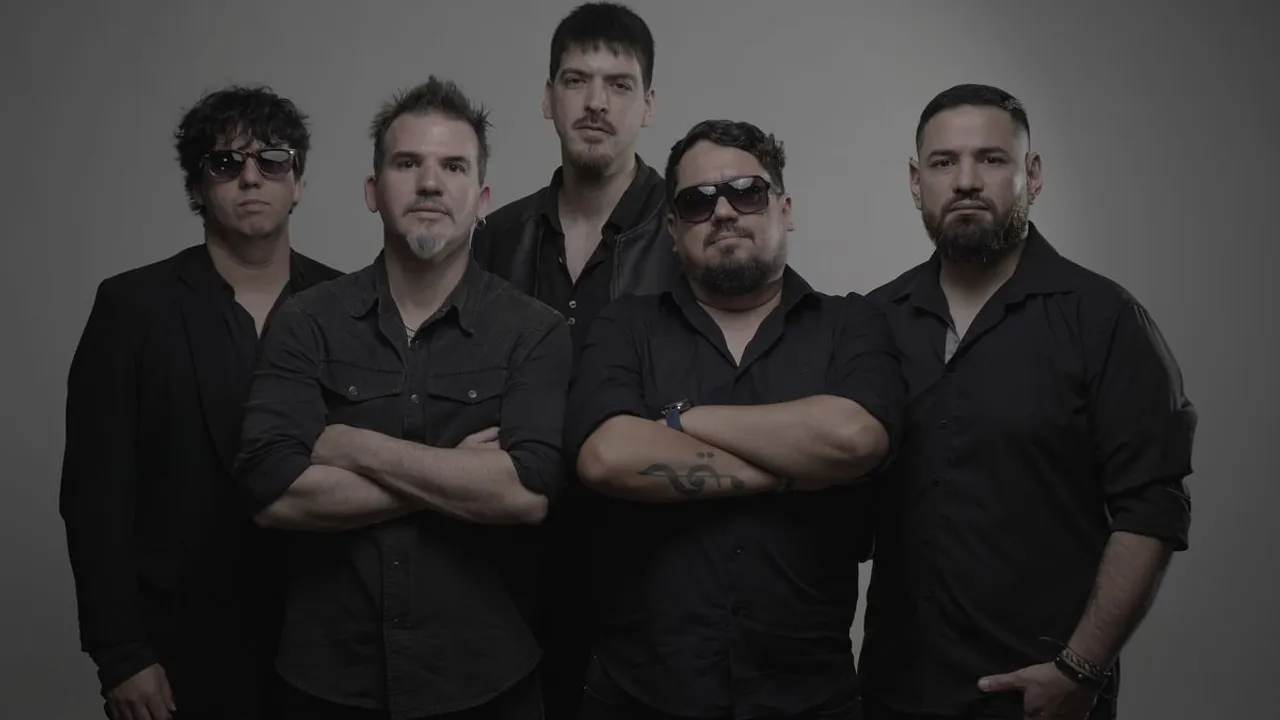 Cinco integrantes vestidos de negro posan juntos mirando al frente sobre un fondo gris en un estudio fotográfico.