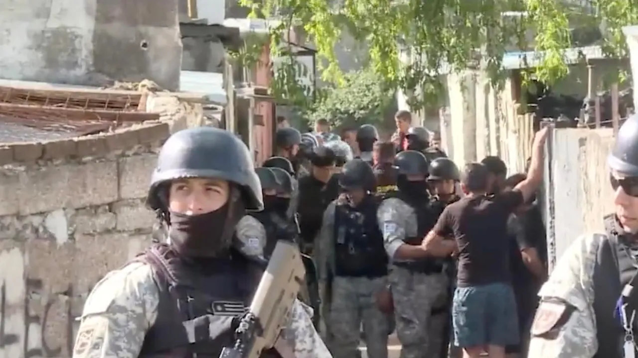 Efectivos policiales con cascos y chalecos tácticos patrullan un pasillo estrecho en una zona residencial urbana.