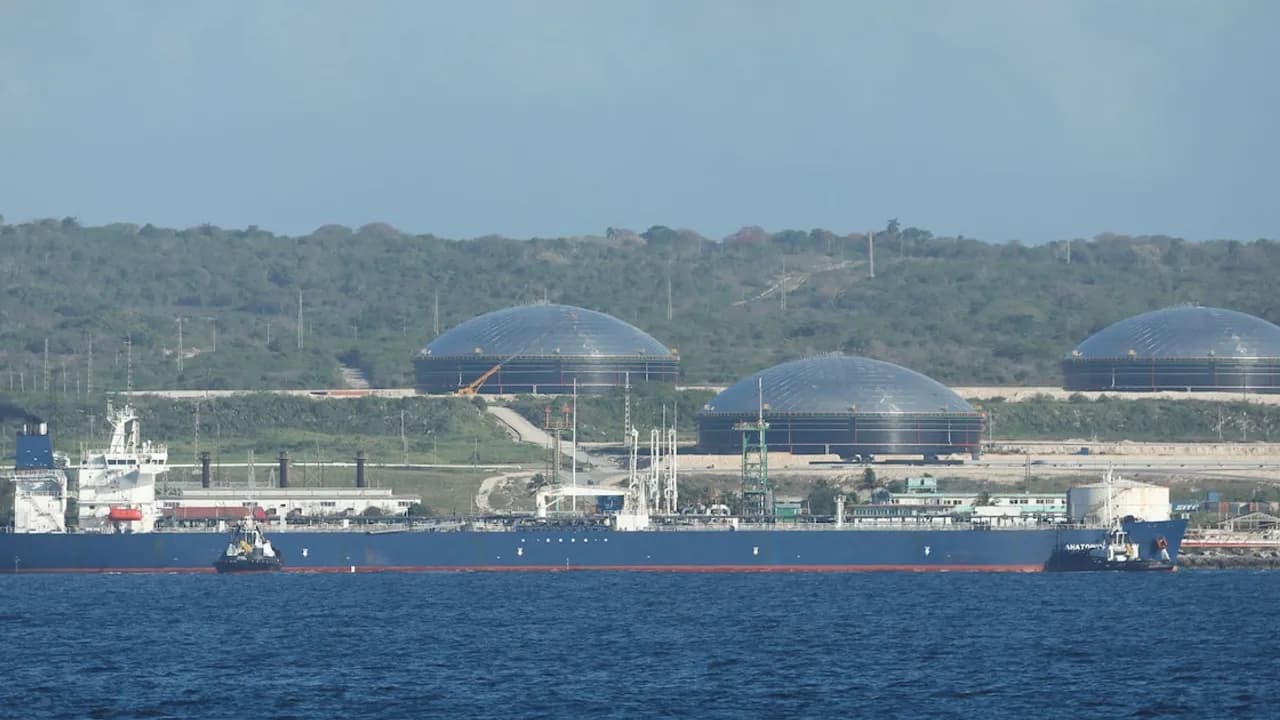 Buque petrolero navega frente a la costa donde se observan varios tanques de almacenamiento con techos de cúpula.