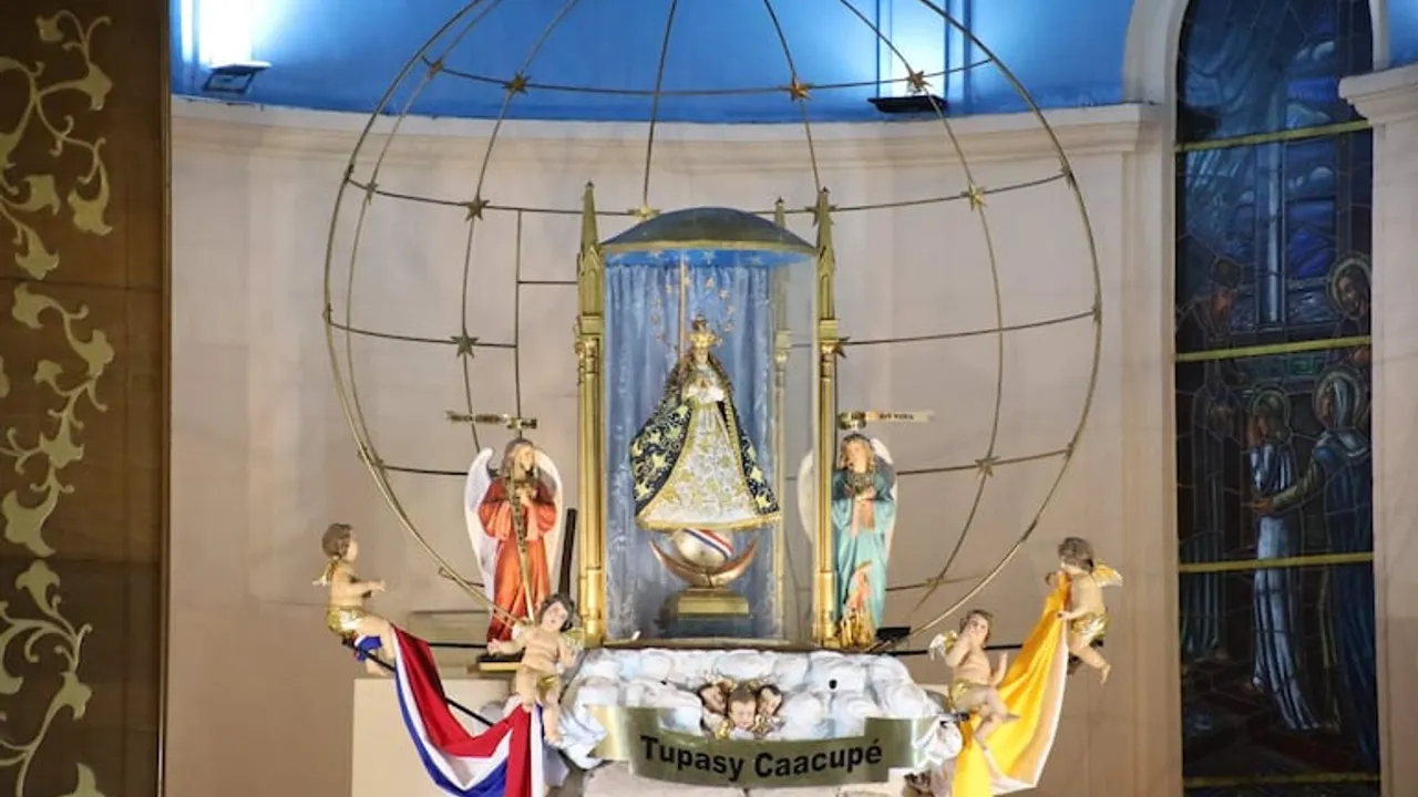 Estatua de la Virgen de Caacupé dentro de un nicho de cristal en el altar mayor junto a figuras de ángeles.