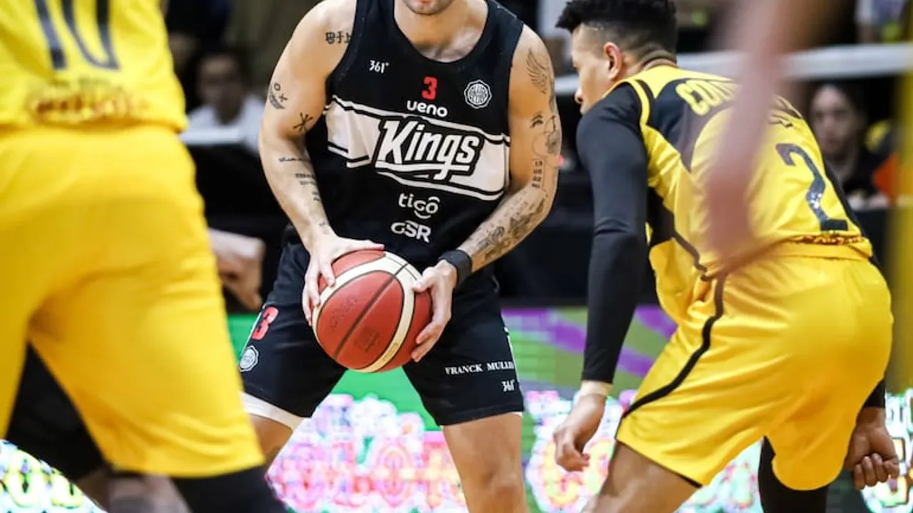 Jugador con camiseta negra del club Olimpia sosteniendo el balón de básquetbol ante la marca de rivales de amarillo.