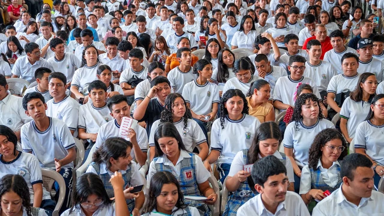 Grupo numeroso de estudiantes sentados en un auditorio con uniformes blancos durante un acto institucional.
