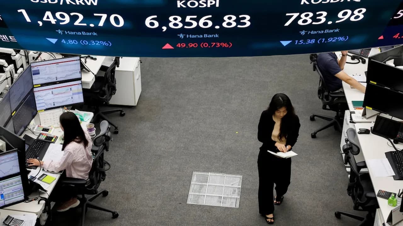 Operadores bursátiles sentados en sus escritorios frente a monitores bajo una gran pantalla con datos del Kospi