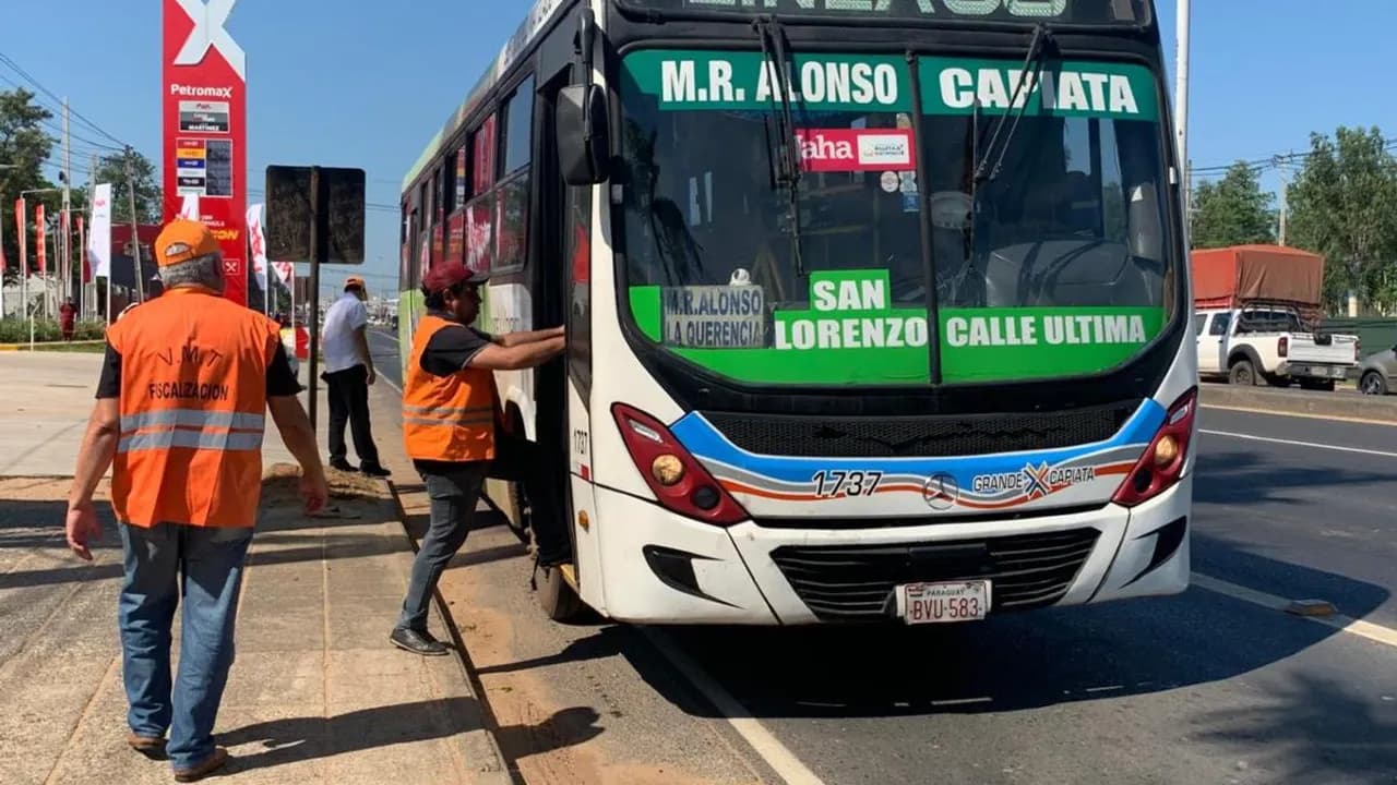 Fiscalizador con chaleco naranja del Viceministerio de Transporte sube a un colectivo en una avenida para verificarlo.