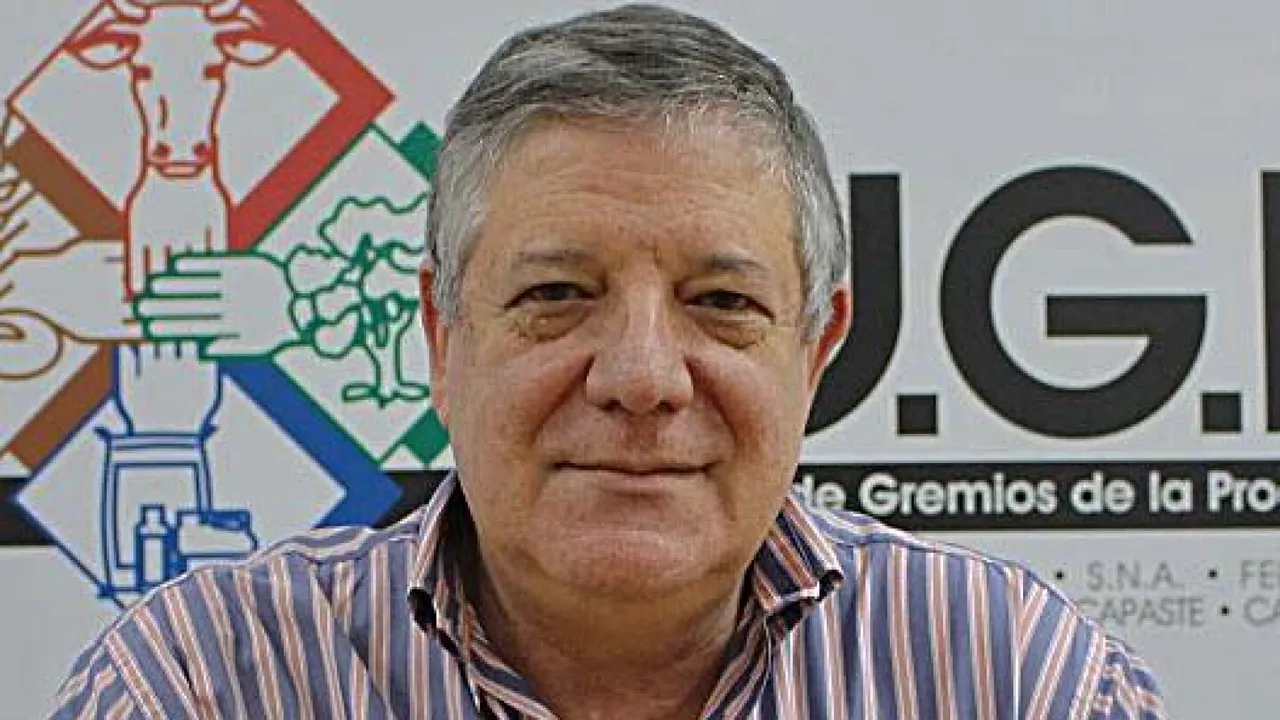 Hombre de cabello canoso y camisa a rayas posa ante la cámara en una oficina con el logotipo de la UGP.