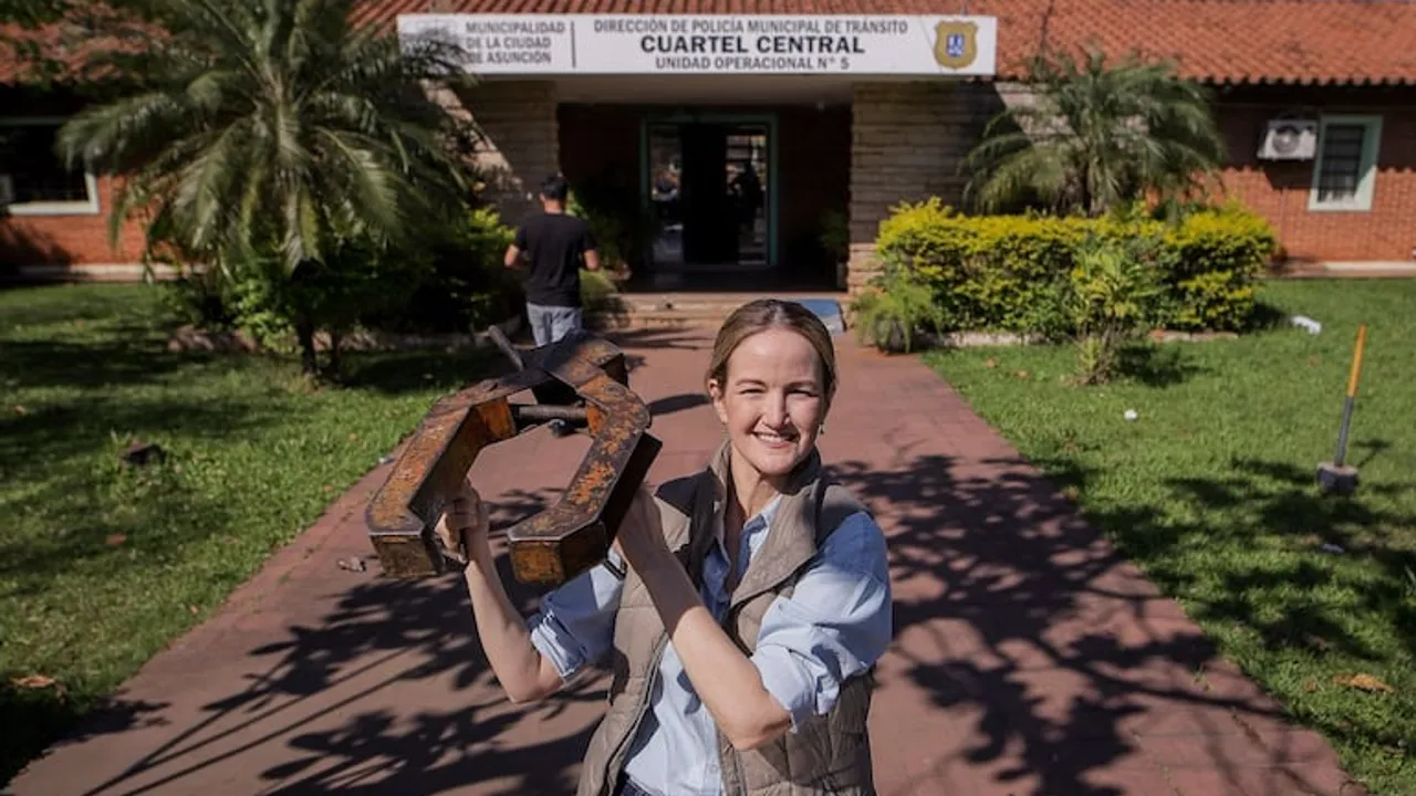 Mujer sonriente sosteniendo un cepo de metal frente al cuartel de la Policía Municipal de Tránsito.