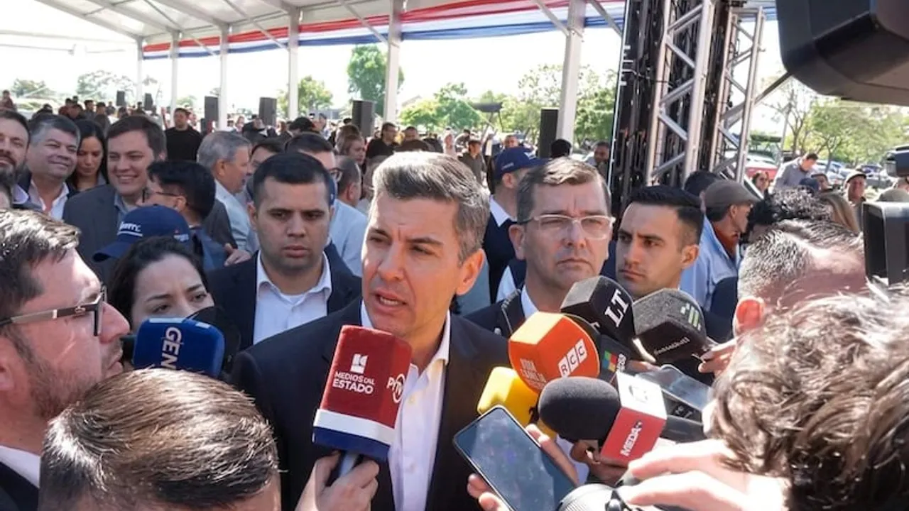 Santiago Peña responde preguntas rodeado de micrófonos de prensa durante un acto oficial al aire libre.