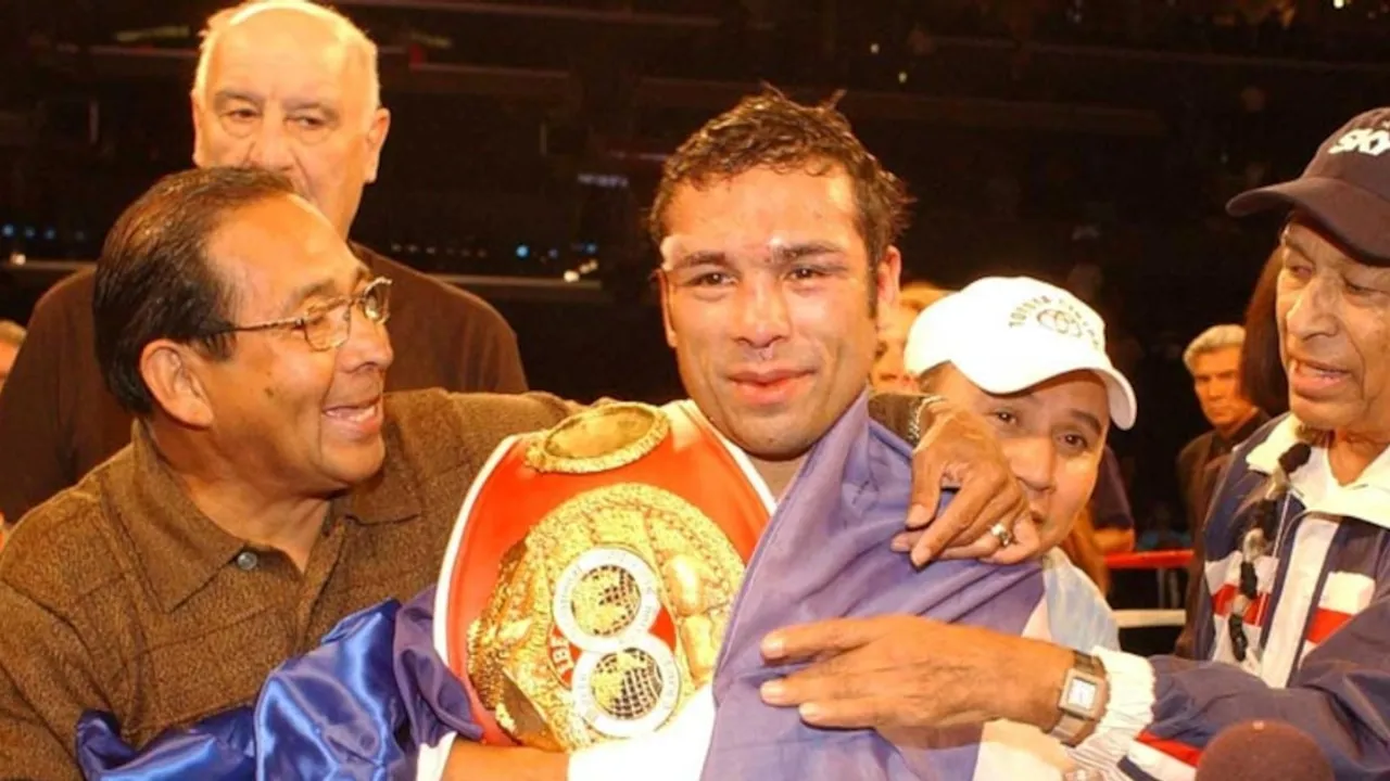 Carlos El Famoso Hernández sonríe en el cuadrilátero con un cinturón de boxeo junto a su equipo.