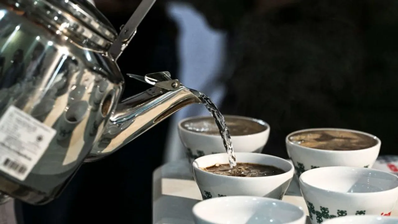 Una pava de metal vierte agua hirviendo dentro de tazas de cerámica dispuestas sobre una mesa.