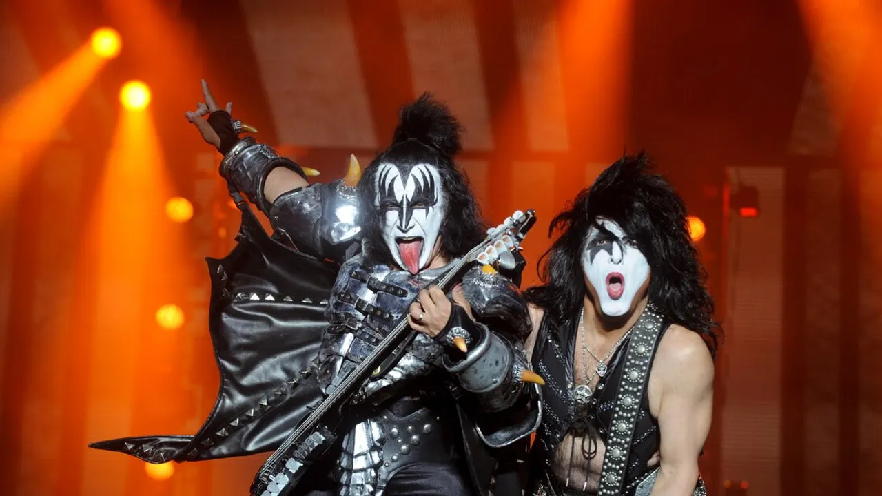 Músicos con maquillaje y trajes de rock posan cantando y tocando la guitarra en un concierto en vivo.