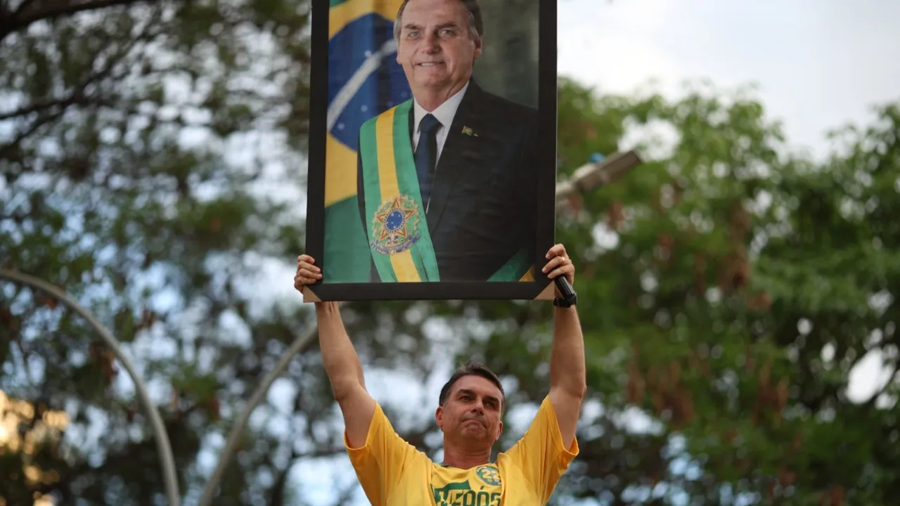 Hombre sostiene en alto un cuadro con el retrato oficial de Jair Bolsonaro con la banda presidencial.