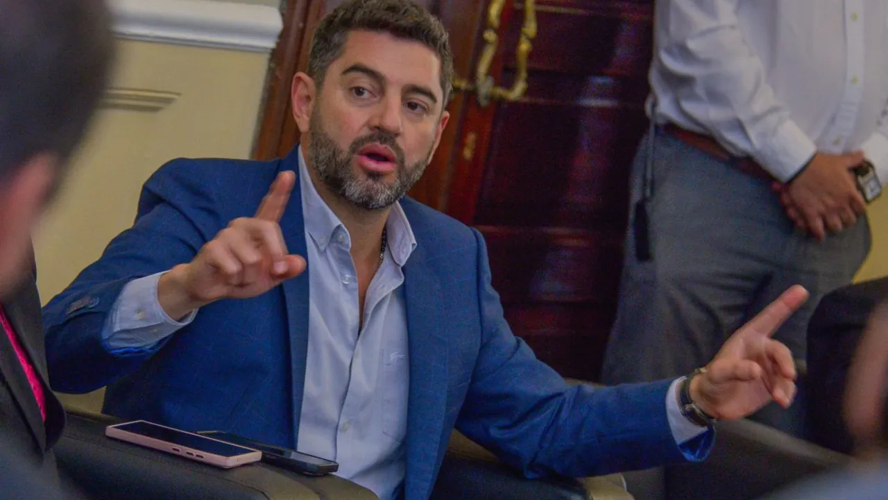 Pedro Alliana gesticula con ambas manos mientras habla en una reunión política, vistiendo saco azul y camisa.