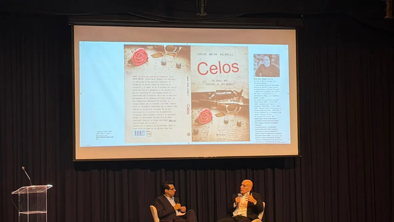 Dos personas conversan sentadas en un escenario frente a una pantalla gigante que proyecta la portada de un libro.