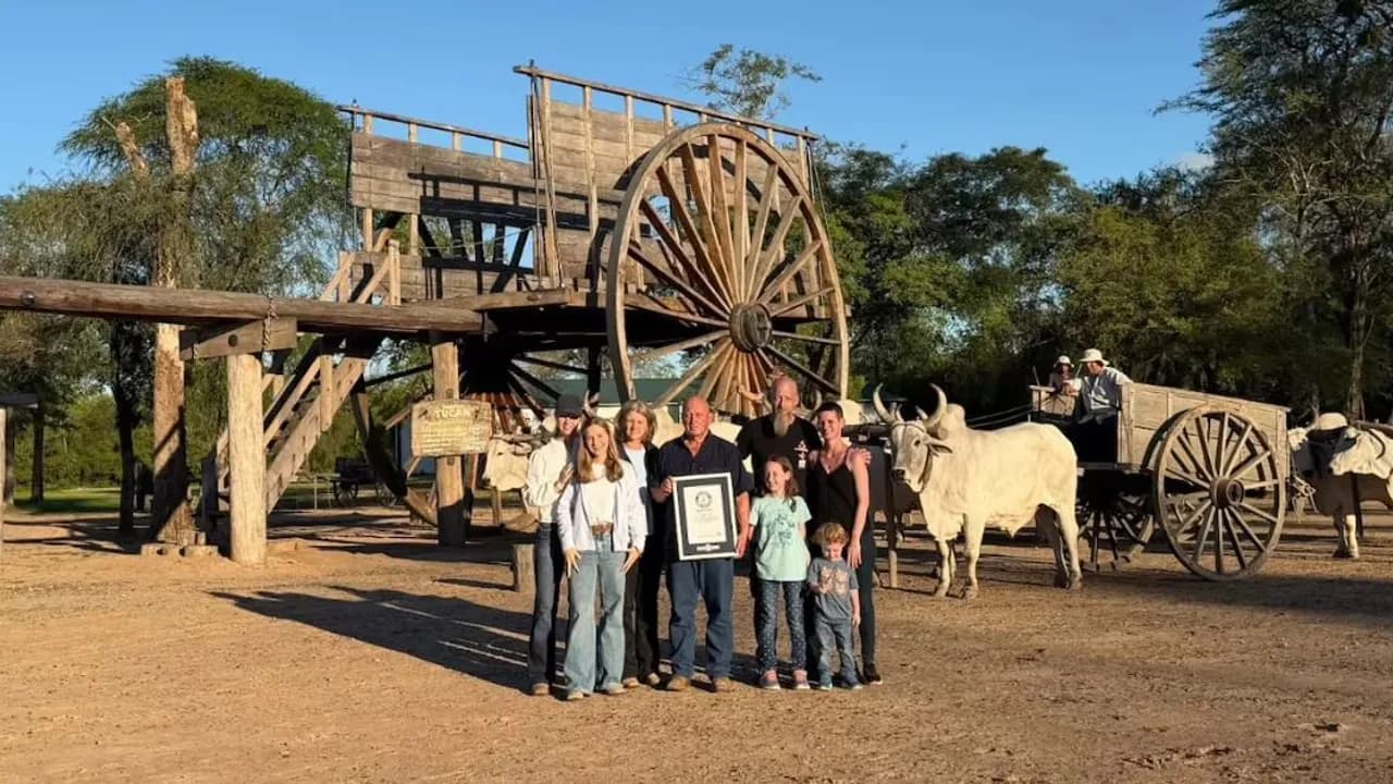 Grupo familiar posa con el certificado de récord Guinness frente a una enorme carreta de madera y bueyes en un rancho.