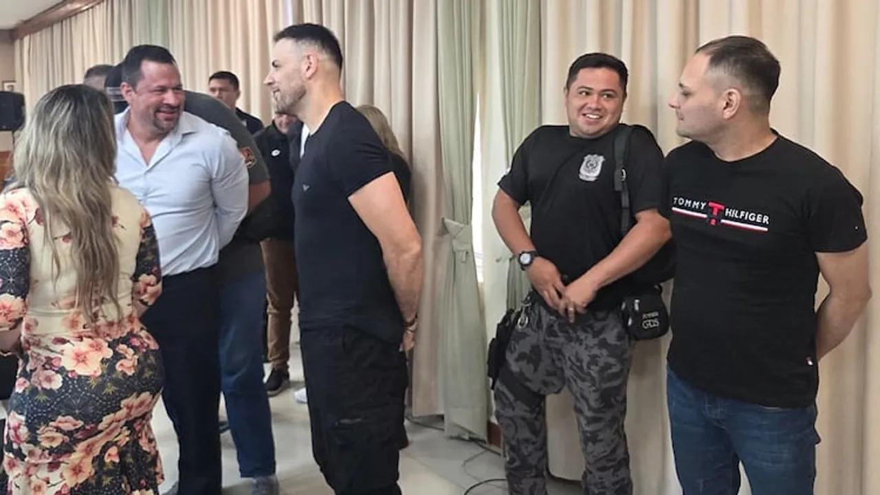 Personas reunidas conversando de pie dentro de una sala judicial con cortinas claras de fondo