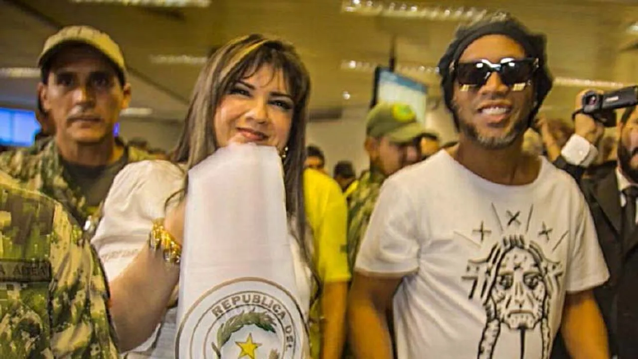 Ronaldinho con gorro negro y gafas oscuras junto a una mujer que sostiene una bandera paraguaya.