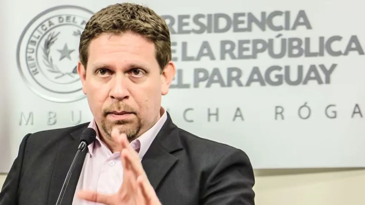 Hombre de traje oscuro habla ante un micrófono frente a un panel oficial que lleva el escudo de Paraguay.