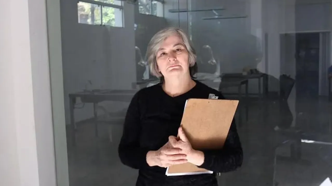 Norma Salinas, agente fiscal, de pie con una carpeta de madera en mano dentro de una oficina con mamparas de vidrio.