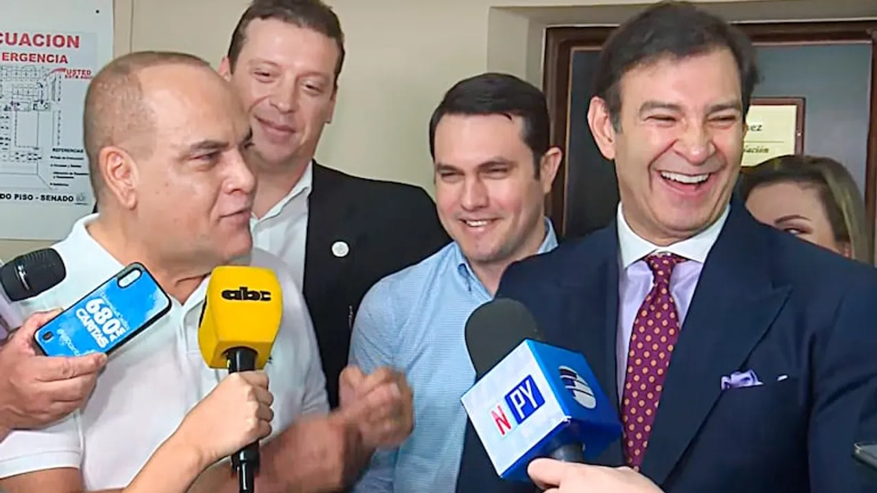 Hernán Rivas sonríe con traje oscuro mientras responde preguntas ante micrófonos de la prensa en el Congreso.