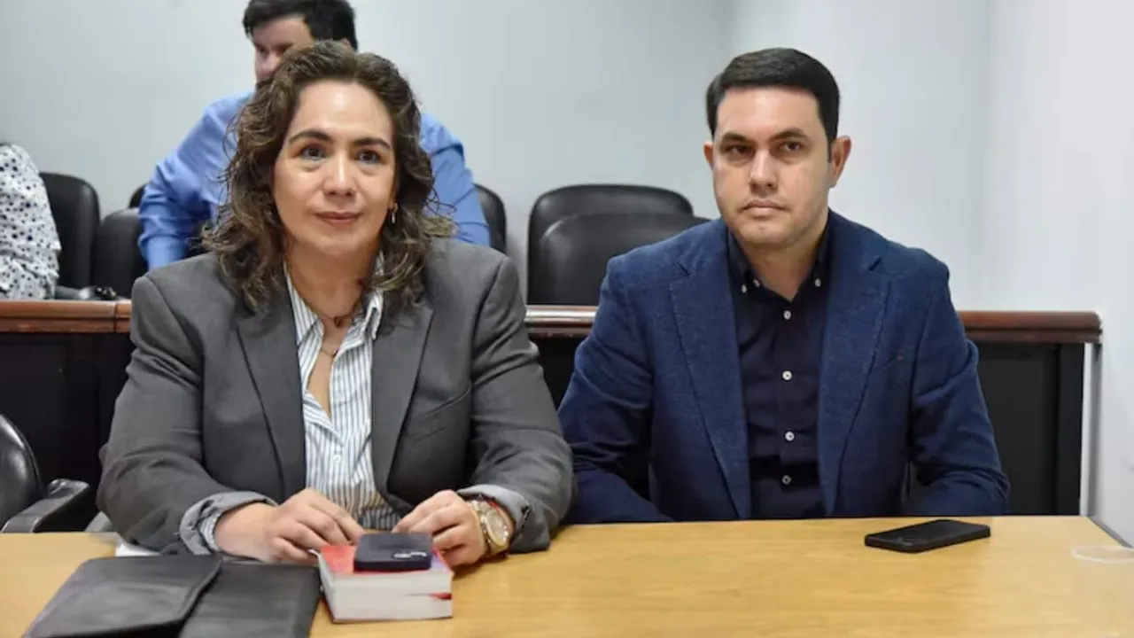 Un hombre y una mujer sentados en una sala judicial detrás de una mesa de audiencias.
