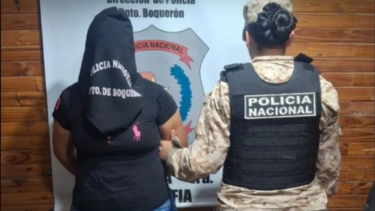 Agente policial custodia de espaldas a una mujer detenida con la cabeza cubierta en una dependencia de Boquerón.