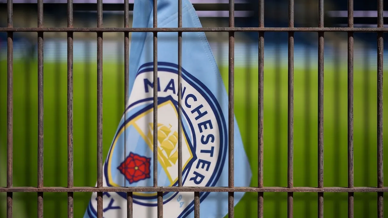 Bandera con el escudo oficial del club de fútbol Manchester City vista detrás de una reja metálica en un estadio.