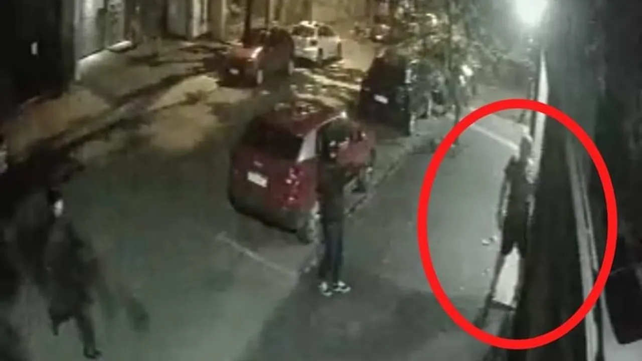 Cámara de seguridad de una calle nocturna donde un círculo rojo señala a un hombre de pie junto a una pared.