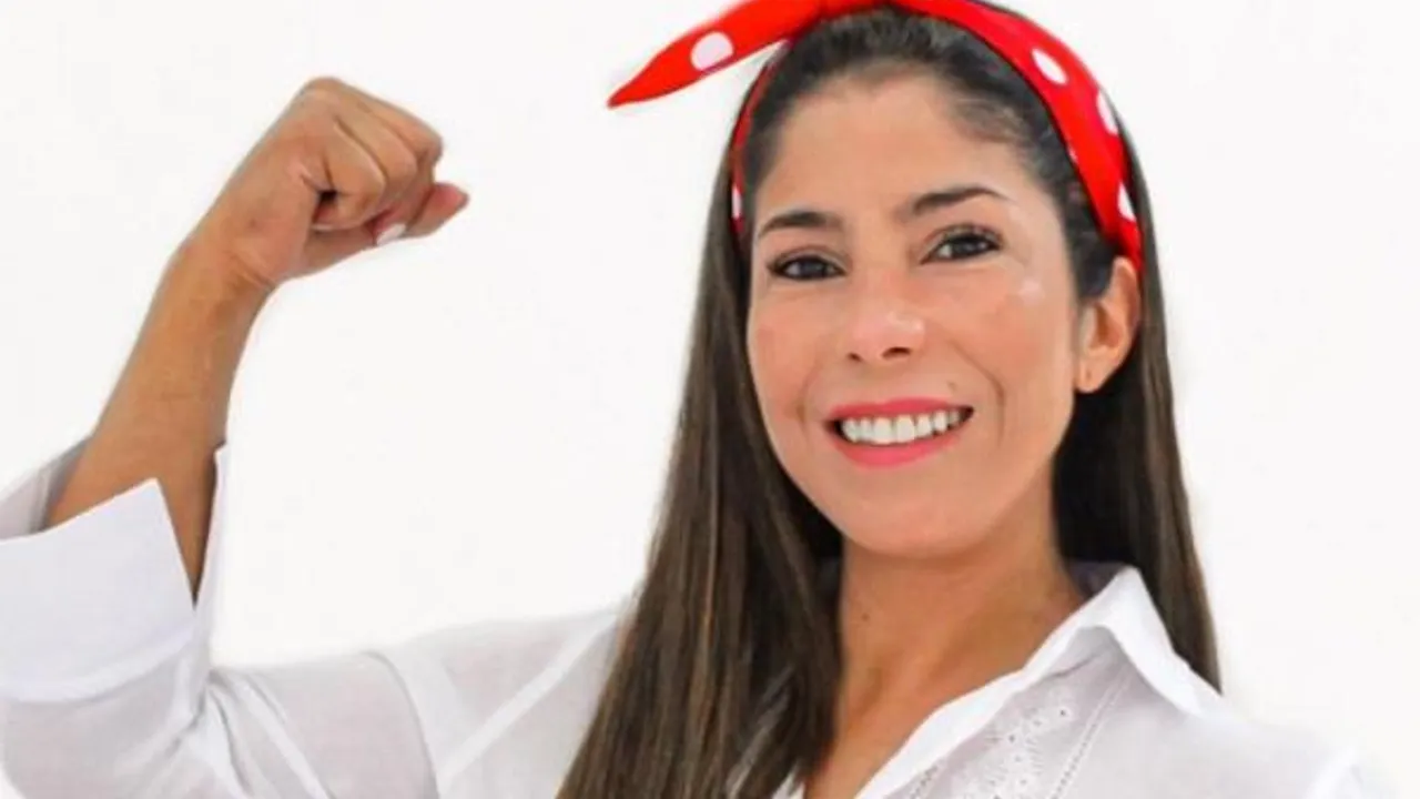 Mujer sonriente con pañuelo rojo a lunares blancos en la cabeza, vestida de blanco y con el puño en alto.