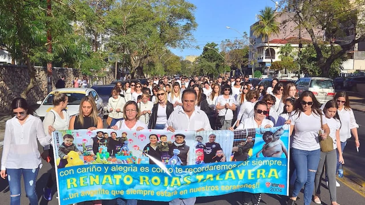 Personas marchando por una calle sostienen un cartel con fotos de un niño y el nombre Renato Rojas Talavera.