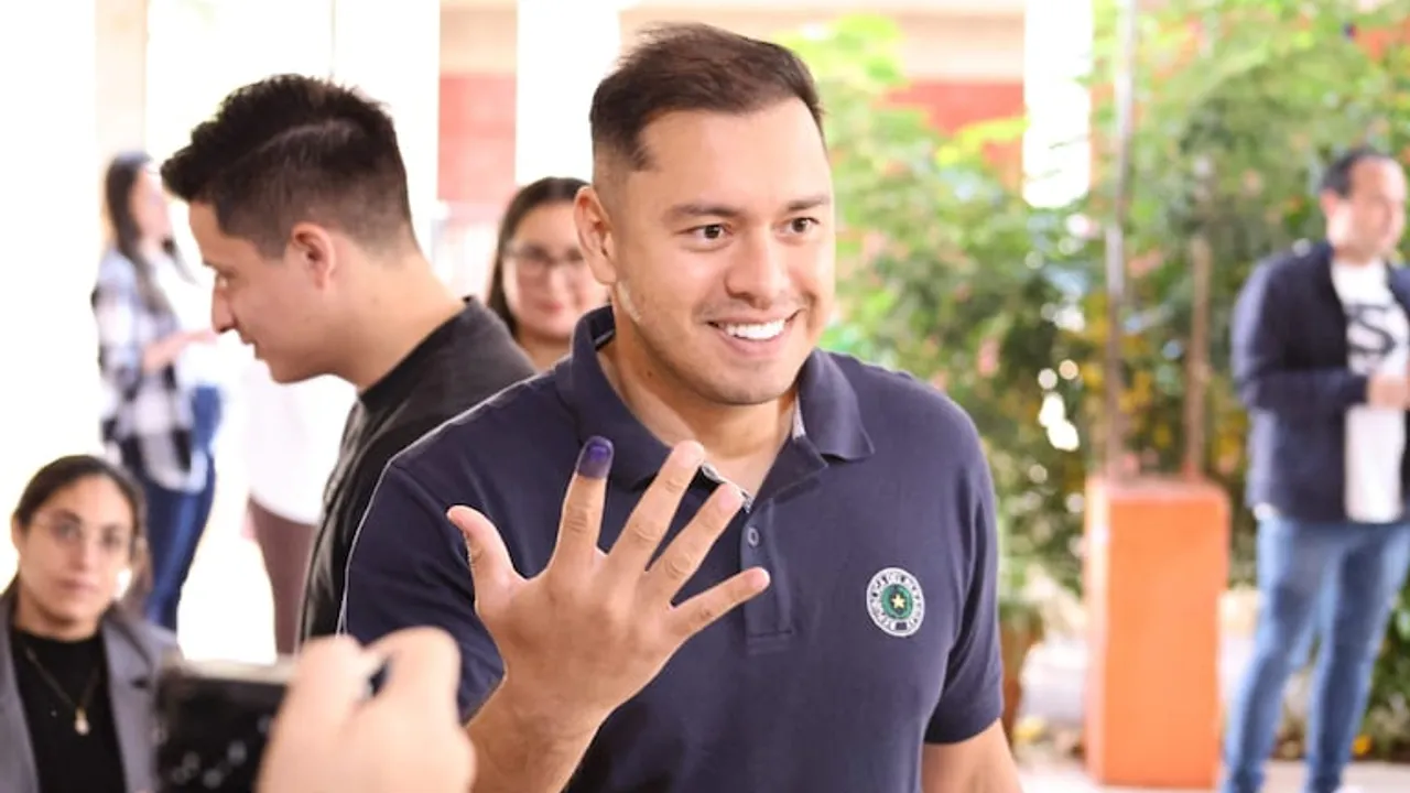 Hombre sonriente con remera oscura muestra su dedo índice entintado tras votar en una jornada cívica.