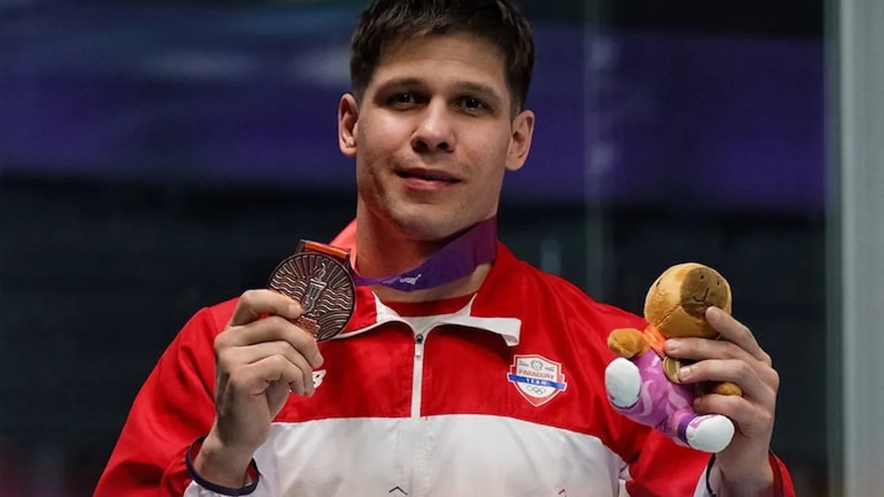 Charles Hockin con campera albirroja sostiene su medalla de bronce y la mascota oficial del torneo.