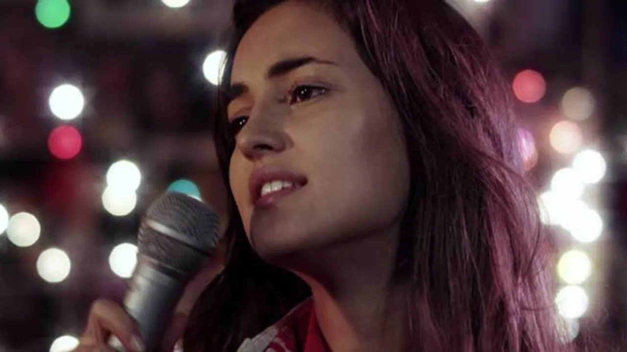 Primer plano de una mujer joven con micrófono en mano cantando frente a un fondo de luces desenfocadas
