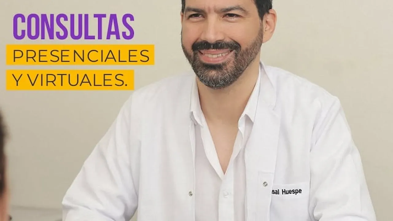 Médico con bata blanca y barba sonríe en un consultorio durante una jornada de atención profesional.