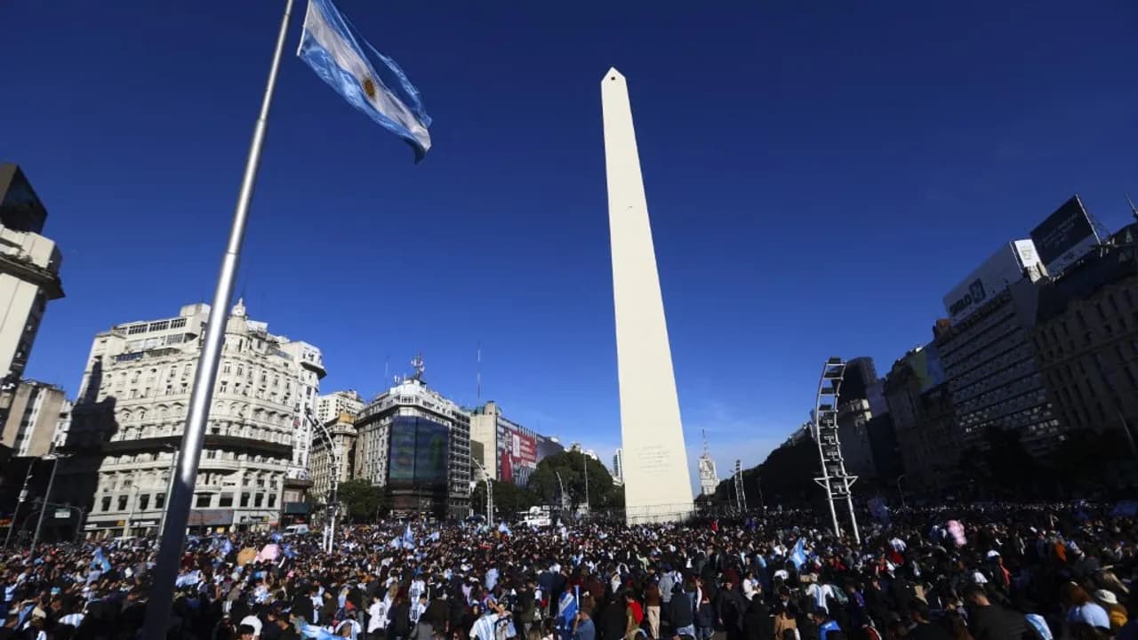 Obelisco de Buenos Aires rodeado por una multitud de personas que portan banderas argentinas bajo un cielo despejado