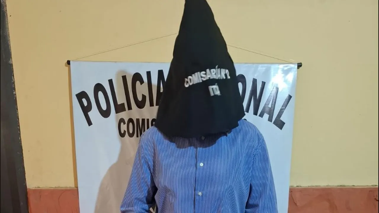 Persona con el rostro cubierto por una capucha negra frente a un cartel de la Policía Nacional en Itá.