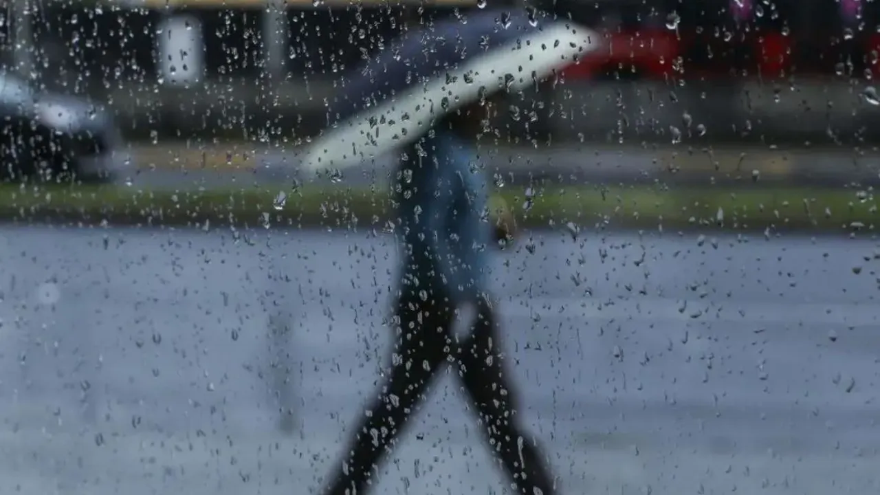 Silueta de un transeúnte con paraguas caminando bajo la lluvia vista a través de un vidrio mojado