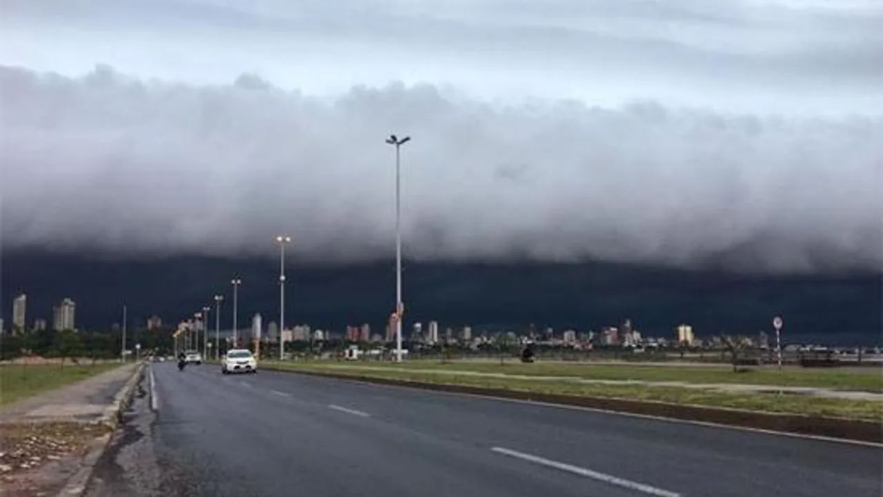 Avenida urbana con automóviles bajo un imponente frente de nubes bajas y densas que cubren el cielo de la ciudad.